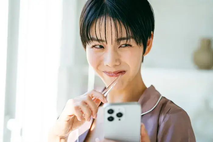 歯磨きをしながらスマートフォンを眺め、明るい表情を浮かべる女性。口元の健康と運気向上のイメージ